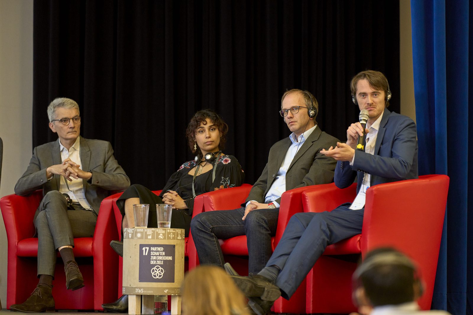 Four people in red armchairs on a stage during a panel discussion.