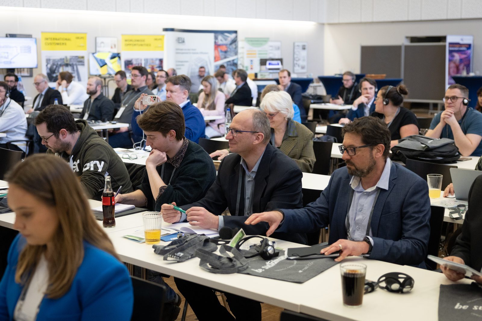 Participants at tables in the hall, some with interpreting headsets.