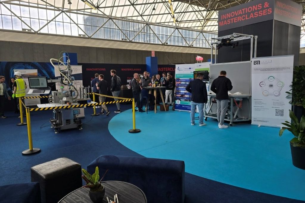 Exhibition area under the hall roof with two robot demonstrators, roll-ups and visitors in front of the sign Innovations and Masterclasses.