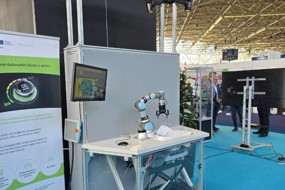 A mobile workstation with a collaborative robot, camera frame and screen next to a PAE-e-green roll-up.