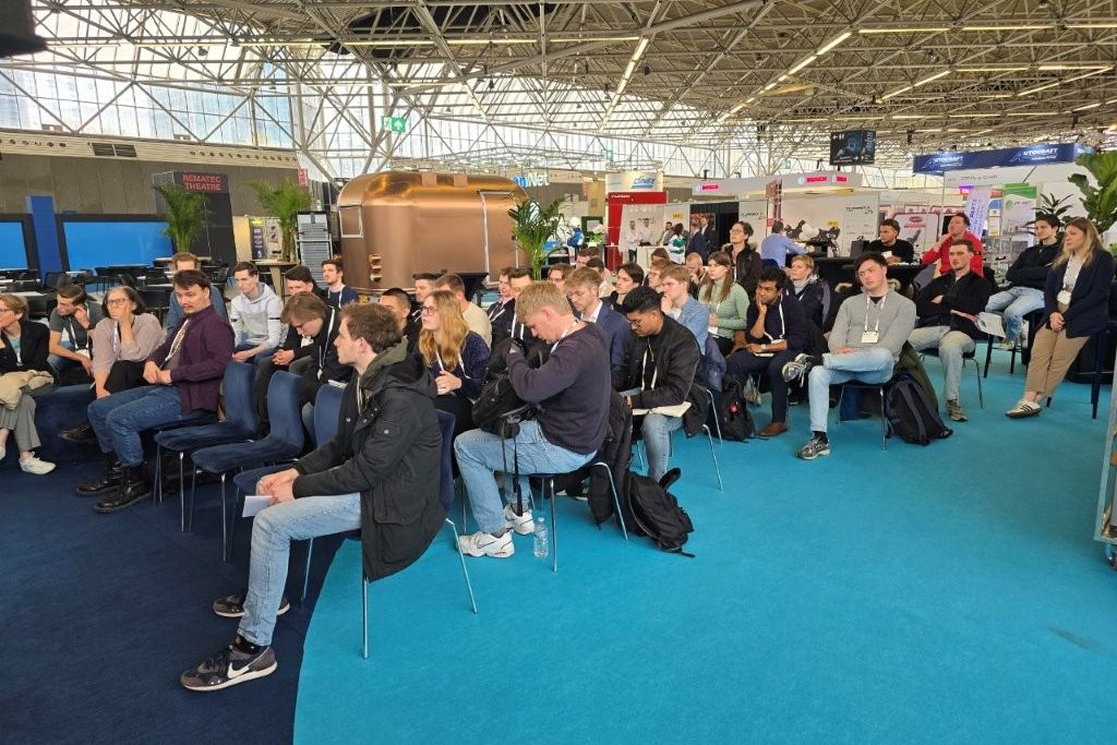 About forty visitors on chairs in the exhibition hall listening to a talk.