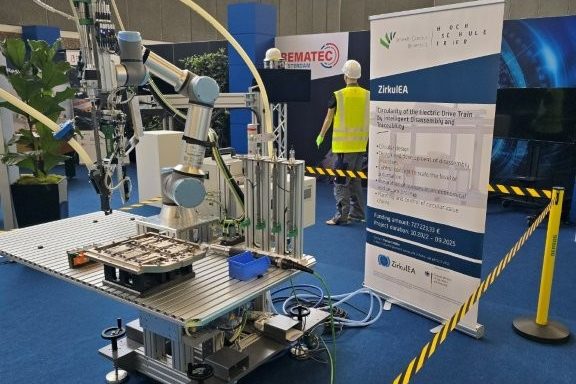 A robot cell with a collaborative robot arm and tools next to a ZirkulEA roll-up, cordoned off with yellow-black tape.