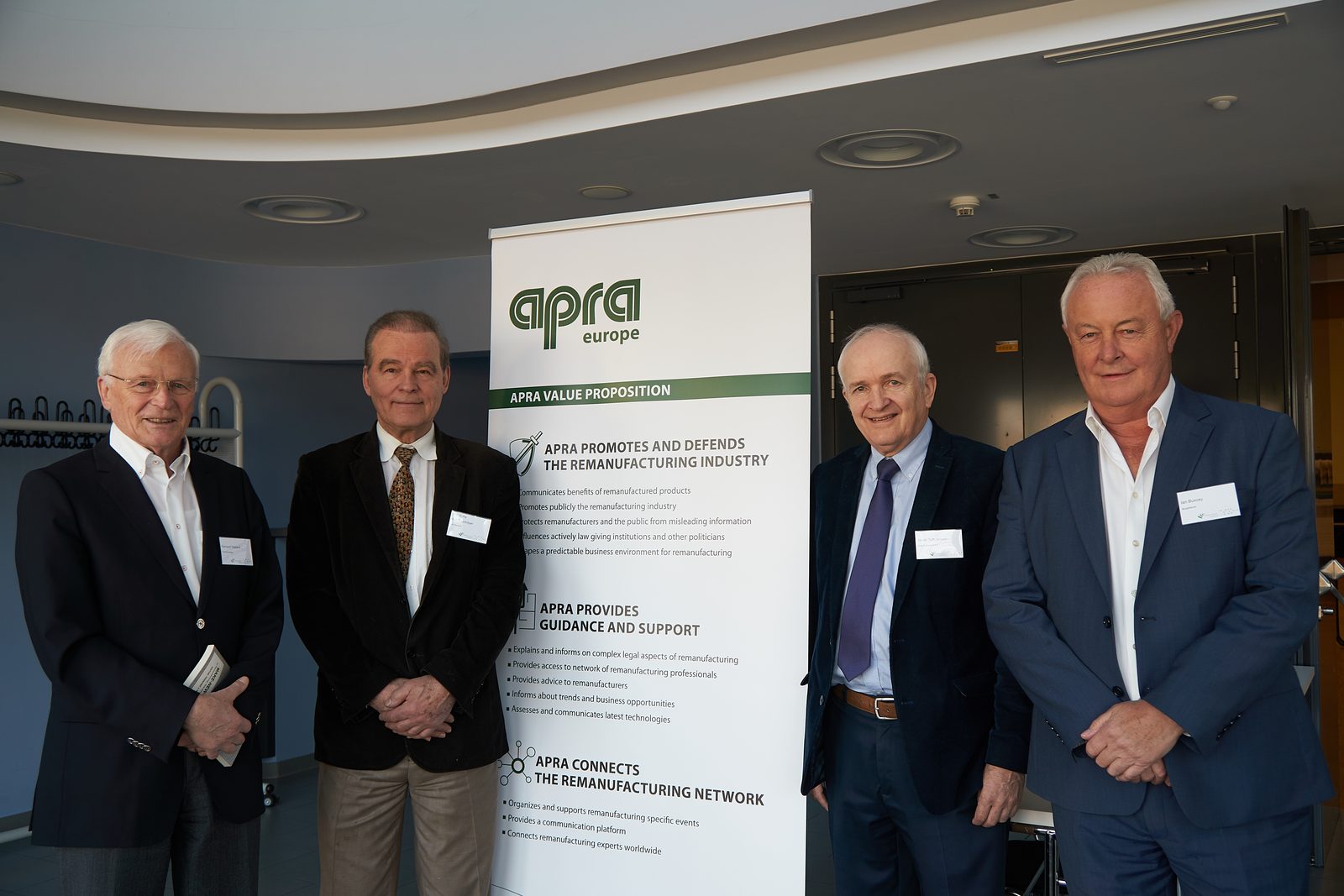 Four men in front of an APRA Europe roll-up.