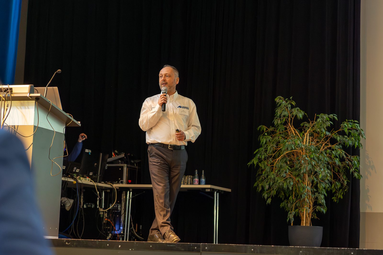 A speaker in a white shirt on stage with a microphone.